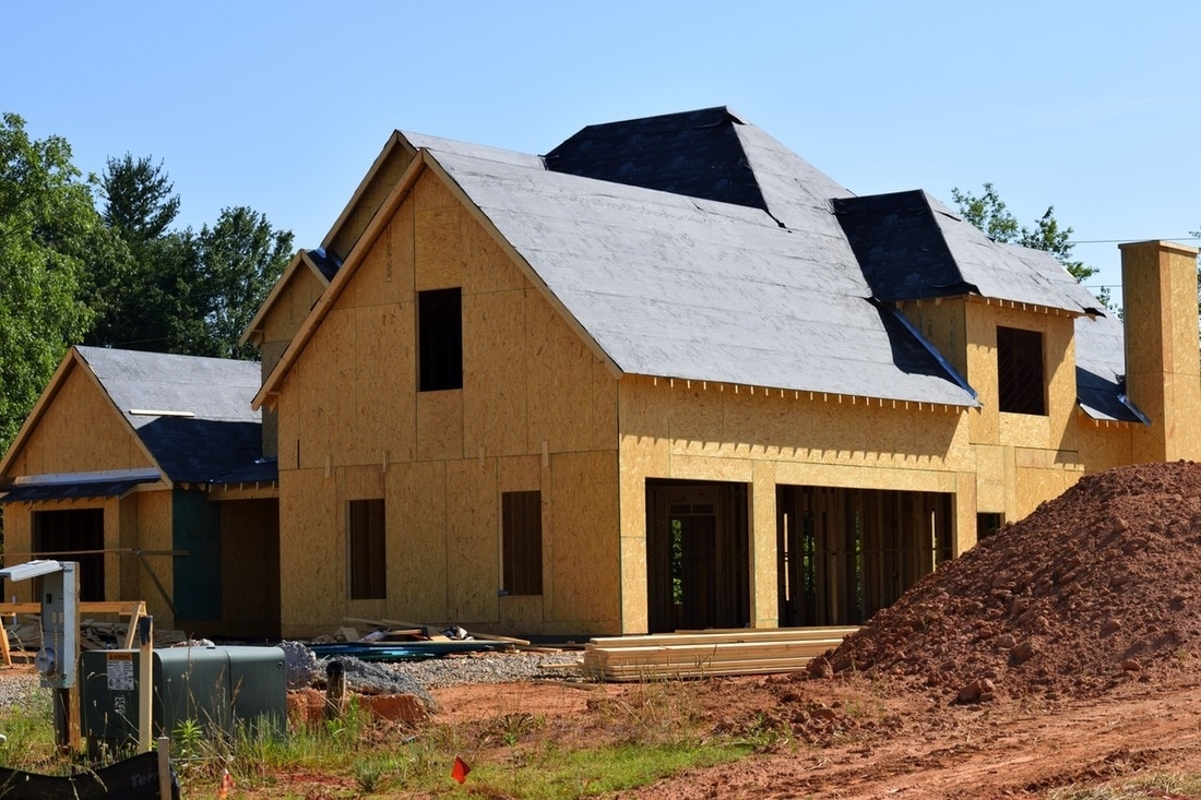 House under construction with wood sheathing, roof underlayment, and earthworks in the foreground