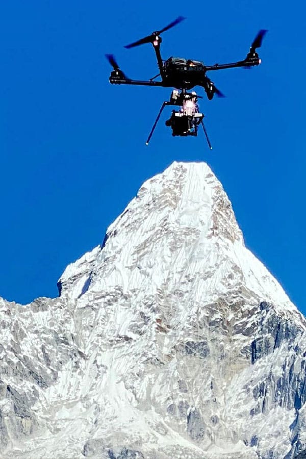Camera-equipped Alta X in flight against a snow-covered mountain and blue sky