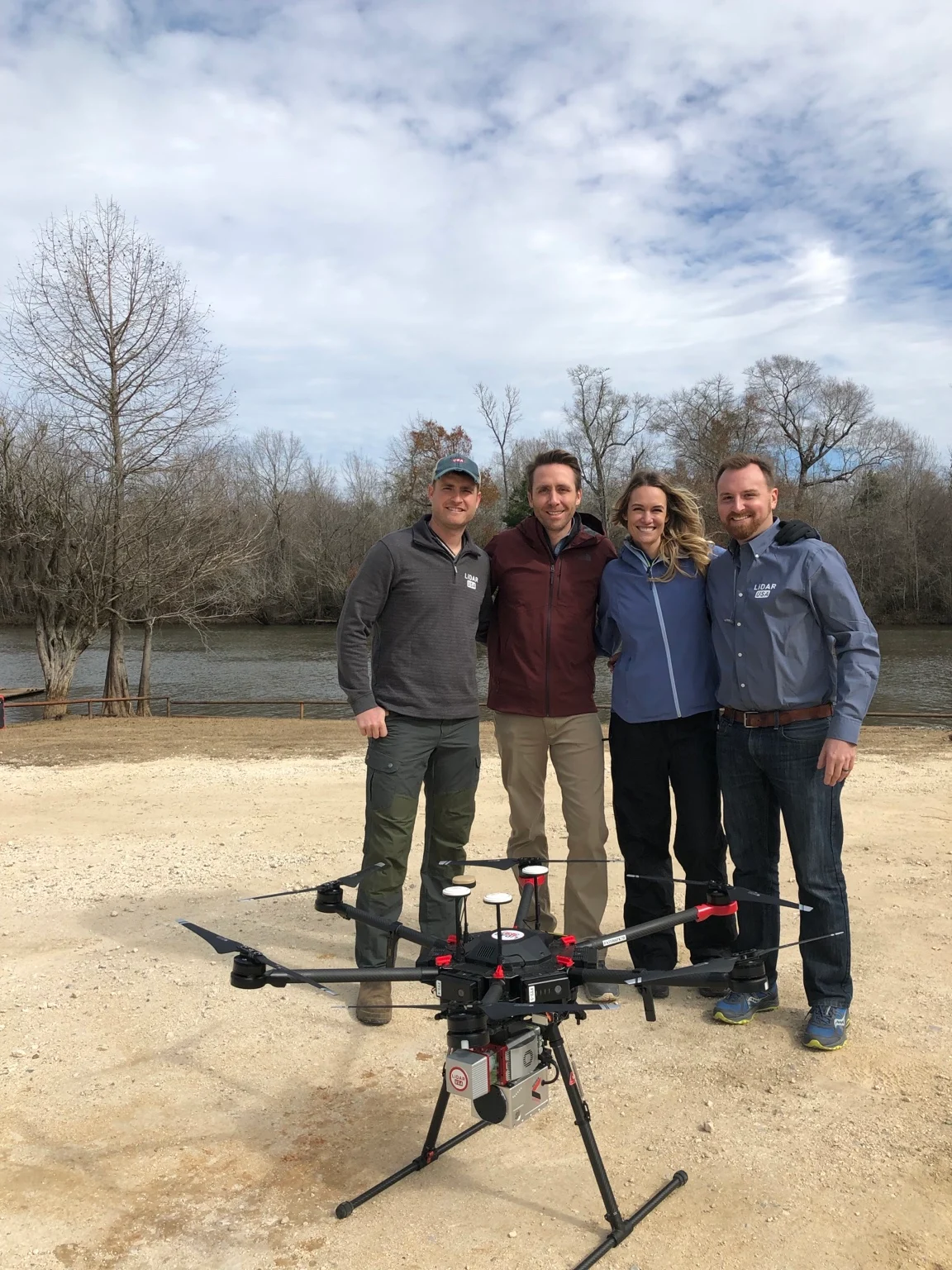 LiDARUSA team with Philippe and Ashlan Cousteau standing behind the LiDAR-equipped UAV beside the river
