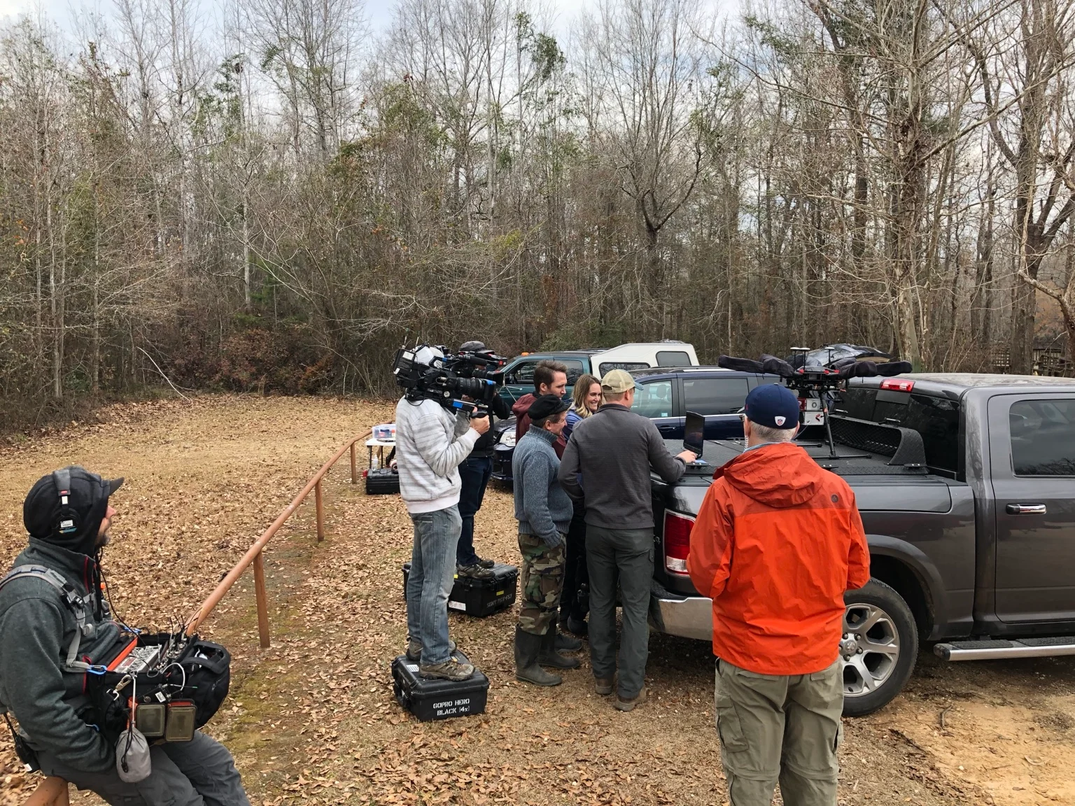 Film crew recording the team reviewing a laptop beside a pickup truck carrying the UAV